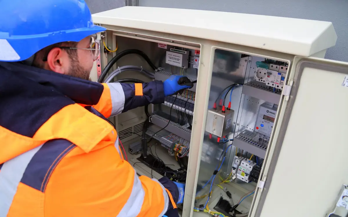 Technician in a hi-vis jacket working inside an outdoor electrical cabinet